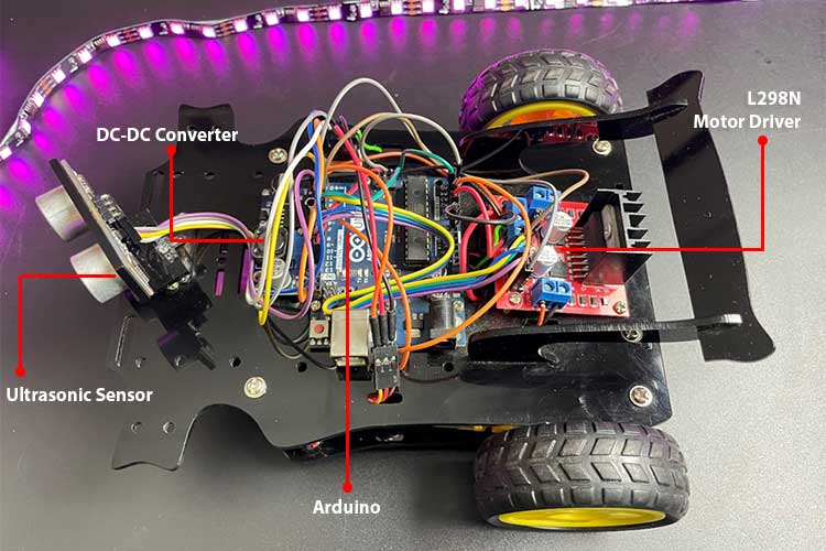 Assembled Arduino obstacle avoiding robot car showing component placement on chassis, professional wiring organization, ultrasonic sensor mounted on servo motor at front, L298N driver secured to upper deck, battery placement, and breadboard connections