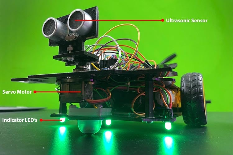 Obstacle avoiding car in operation showing RGB LED indicators illuminated green for forward movement, navigating around obstacles with ultrasonic sensor mounted on servo scanning ahead